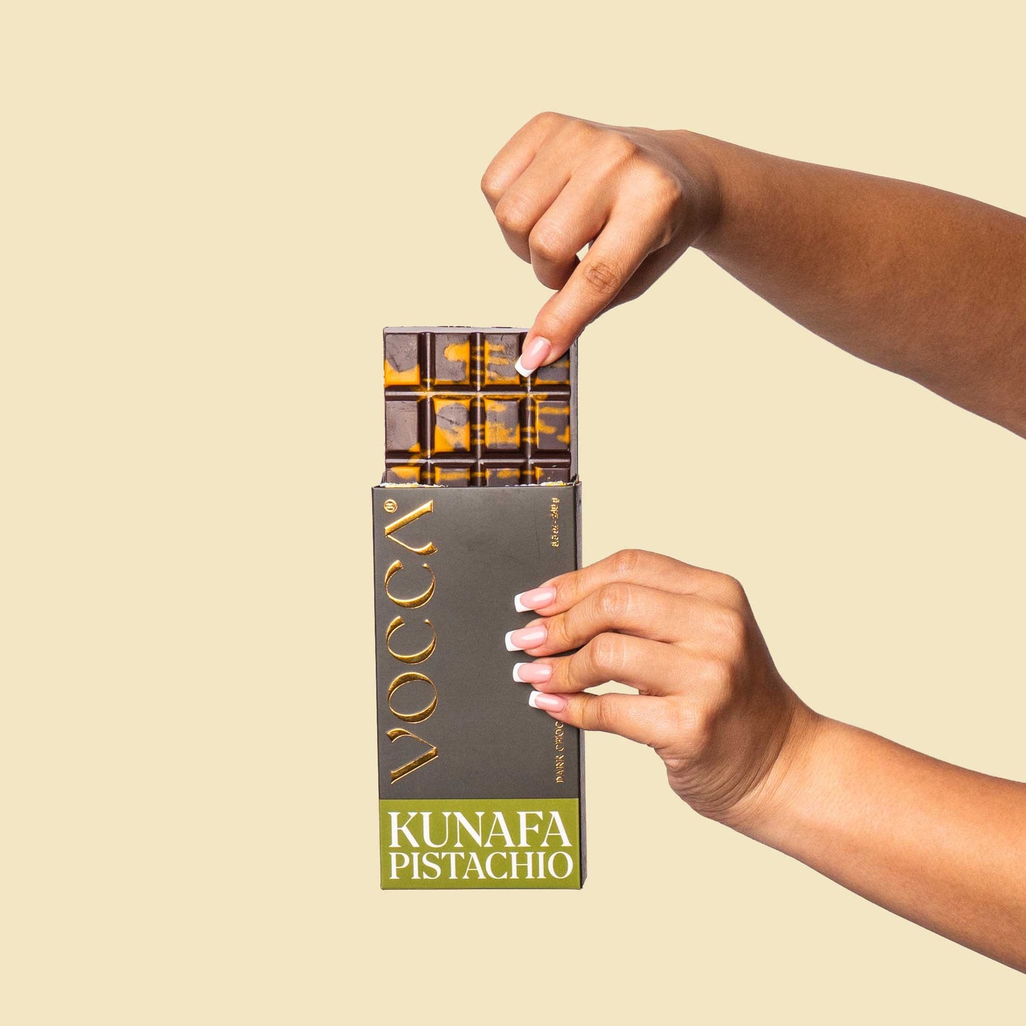 Hand holding a VOCCA Kunafa Pistachio chocolate bar against a beige background