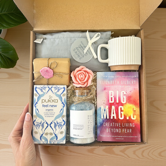Open gift box with various items including a mug, soap, and book on a wooden surface.