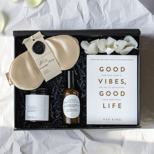 Gift set with eye mask, candle, and bottle on crumpled paper with flowers.